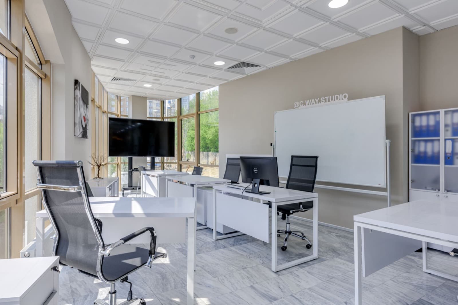 An empty open-plan office with white desks and swivel chairs.